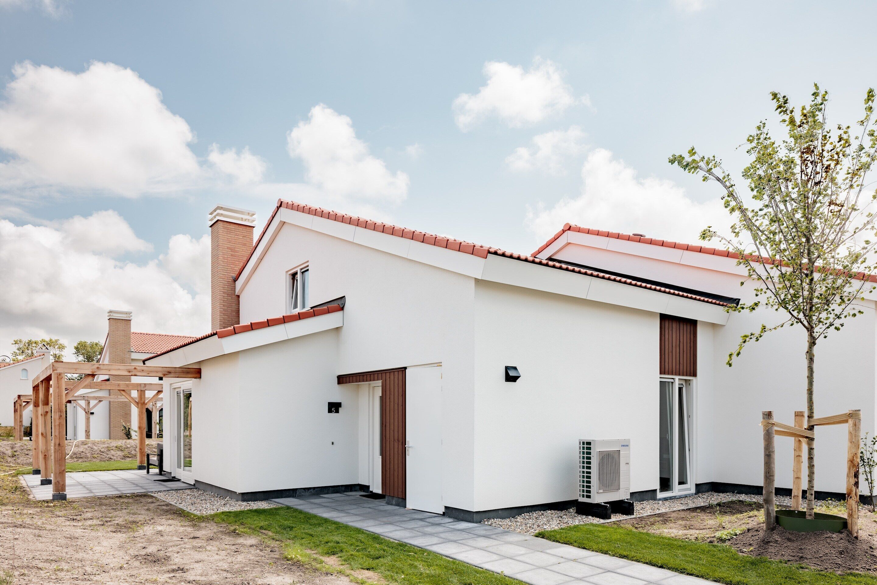 Una casa moderna con fachada blanca, techo de tejas rojas y un pequeño jardín.