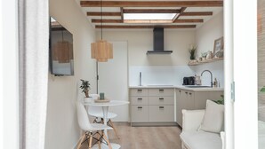 Een compacte keuken met witte kastjes, een eethoek met een ronde tafel en stoelen, en een bank.