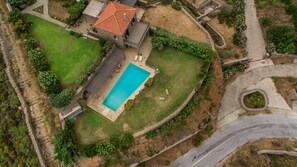 An aerial view of a property with a swimming pool, stone pathway, and a house with a red-tiled roof.
