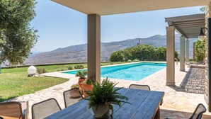 Un patio au bord de la piscine, doté d’un espace salon extérieur, d’une pergola et offrant une vue sur les montagnes.