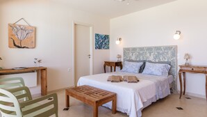 Une chambre à coucher comprenant un lit, des tables de chevet, un bureau, des chaises, un ventilateur de plafond et des œuvres d’art accrochées aux murs.