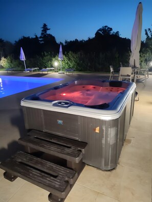 Un jacuzzi con banco incorporado, una piscina y mobiliario de exterior.