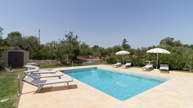 A rectangular swimming pool with clear blue water, surrounded by beige tiles. There are several lounge chairs and umbrellas along the poolside. - Corallo House - Alba Rossa Room with Shared Pool, Wi-Fi and Air Conditioning (Polignano a Mare)