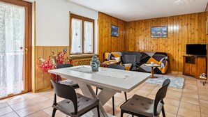 A room with a wooden paneled wall, a sofa, a TV, and a dining table with chairs. - Apartment 'Appartamento Vioz' with Mountain View and Balcony (Peio)