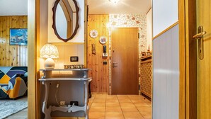A hallway with a wooden door, a mirror, a table with a lamp, and a bed with a patterned bedspread. - Apartment 'Appartamento Vioz' with Mountain View and Balcony (Peio)