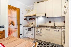 A modern kitchen with white cabinets, a built-in oven, a sink, and a dining area with a wooden table. - Apartment 'Appartamento Vioz' with Mountain View and Balcony (Peio)