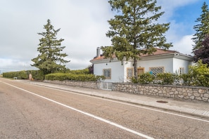 A two-story white building with a red-tiled roof, a stone wall, and a paved sidewalk.