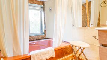 Une salle de bain avec une baignoire, une fenêtre, un miroir et une serviette sur le sol.