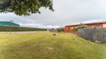 A grassy yard with a swing set, a red building, and a green structure in the background.