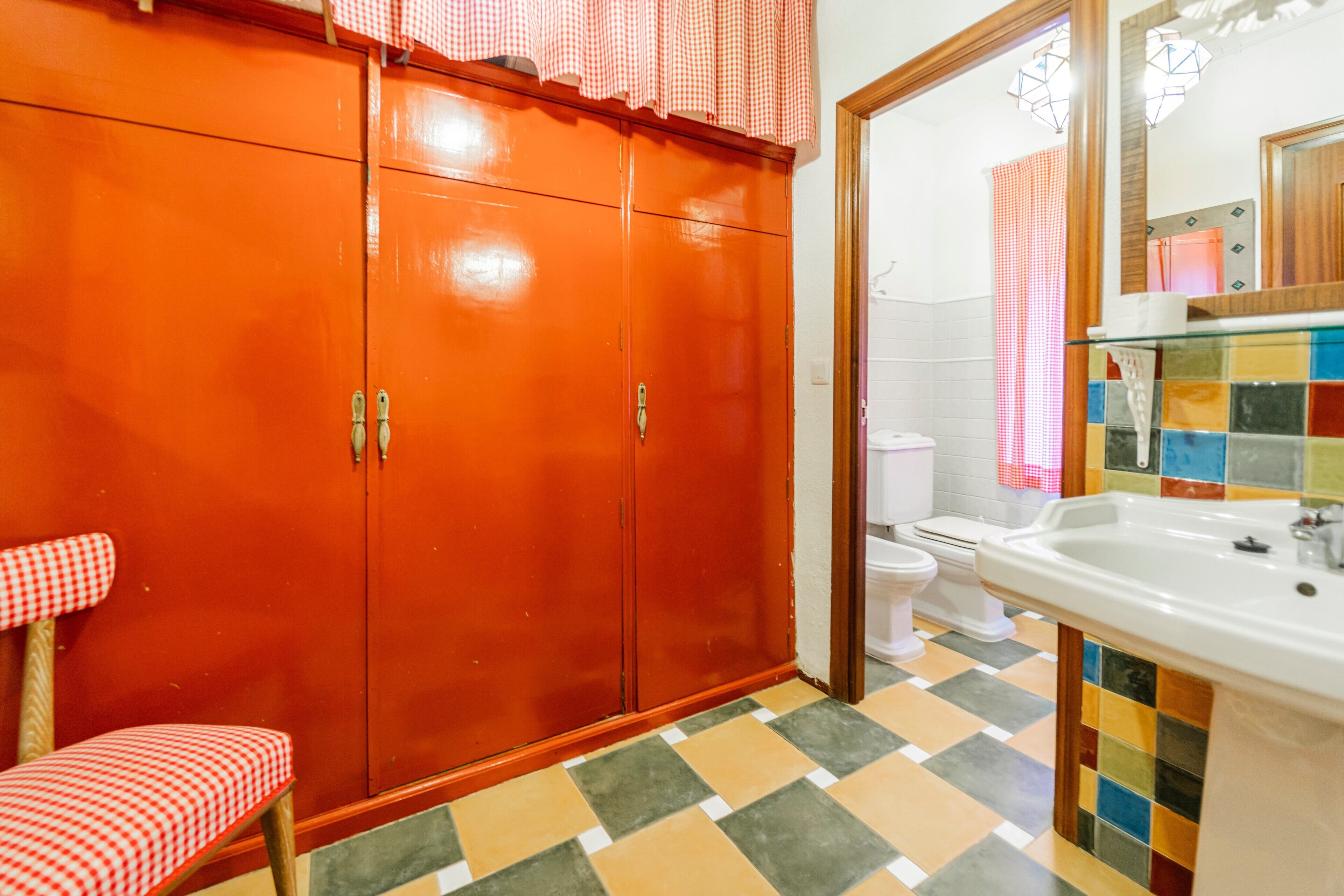 A bathroom with a checkered chair, a sink, a toilet, and a mirror.