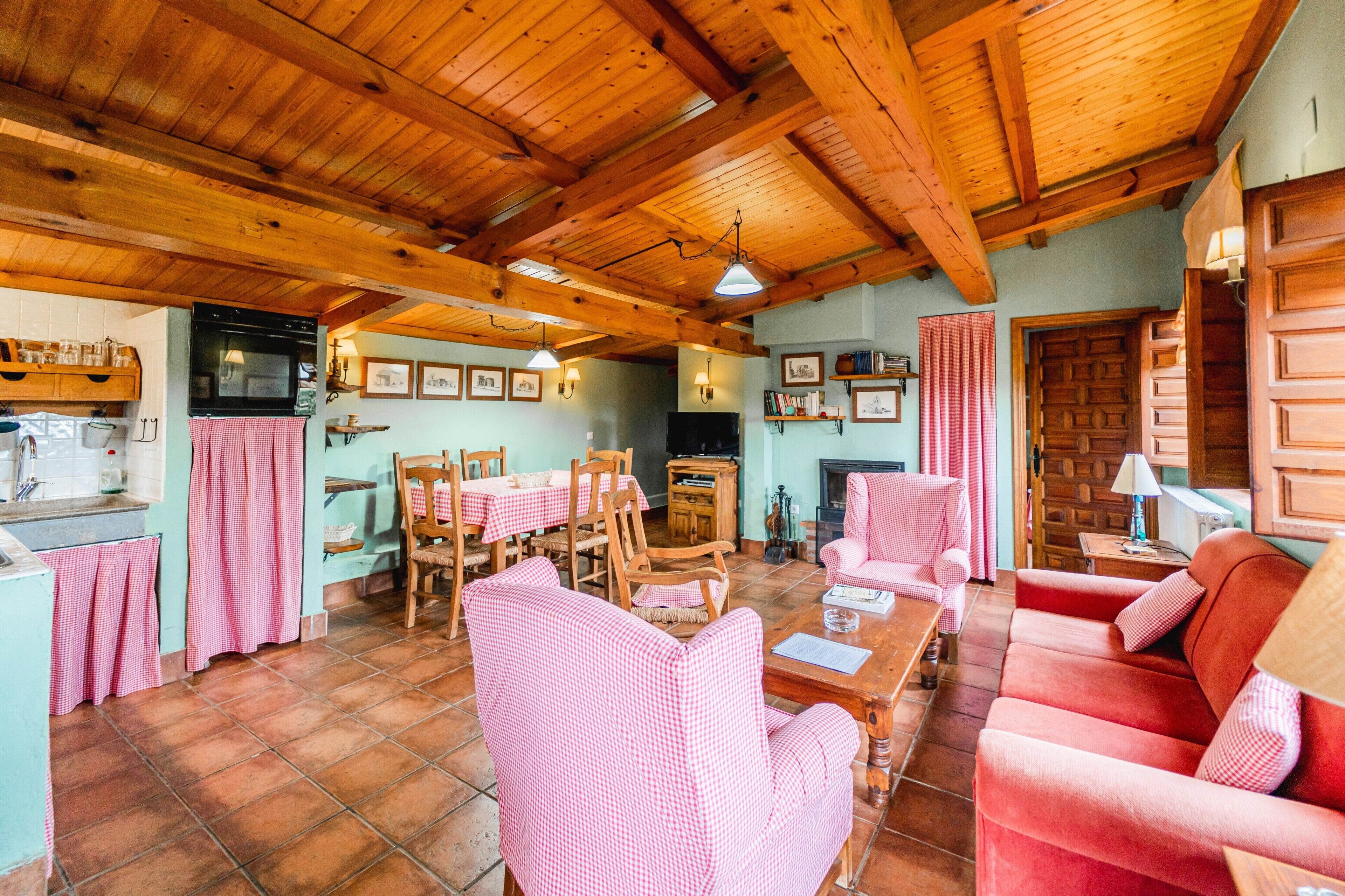 Un intérieur chaleureux avec un plafond en bois, un coin repas avec des nappes à carreaux et un canapé rouge.