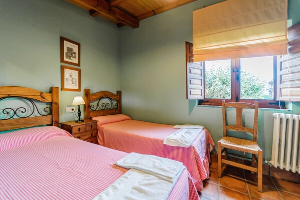A room with two beds, a chair, a table with a lamp, and a window with a view.