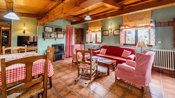 A cozy living room with wooden beams, a red sofa, checkered chairs, a fireplace, and a television. - Country House 'El Gallinero' with Mountain View and Private Garden (Castrejón de la Peña)