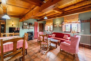 A cozy living room with wooden beams, a red sofa, checkered chairs, a fireplace, and a television.