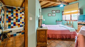 A room with a checkered bedspread, a wooden nightstand, a window with a view, and a tiled wall. - Country House 'El Gallinero' with Mountain View and Private Garden (Castrejón de la Peña)