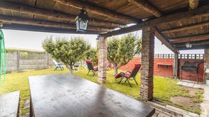 An outdoor patio with a wooden table and chairs, a brick pillar, and a grill. - Country House 'El Gallinero' with Mountain View and Private Garden (Castrejón de la Peña)