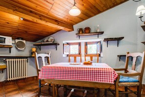 A dining area with a checkered tablecloth, wooden chairs, a window with shutters, and a wooden ceiling.
