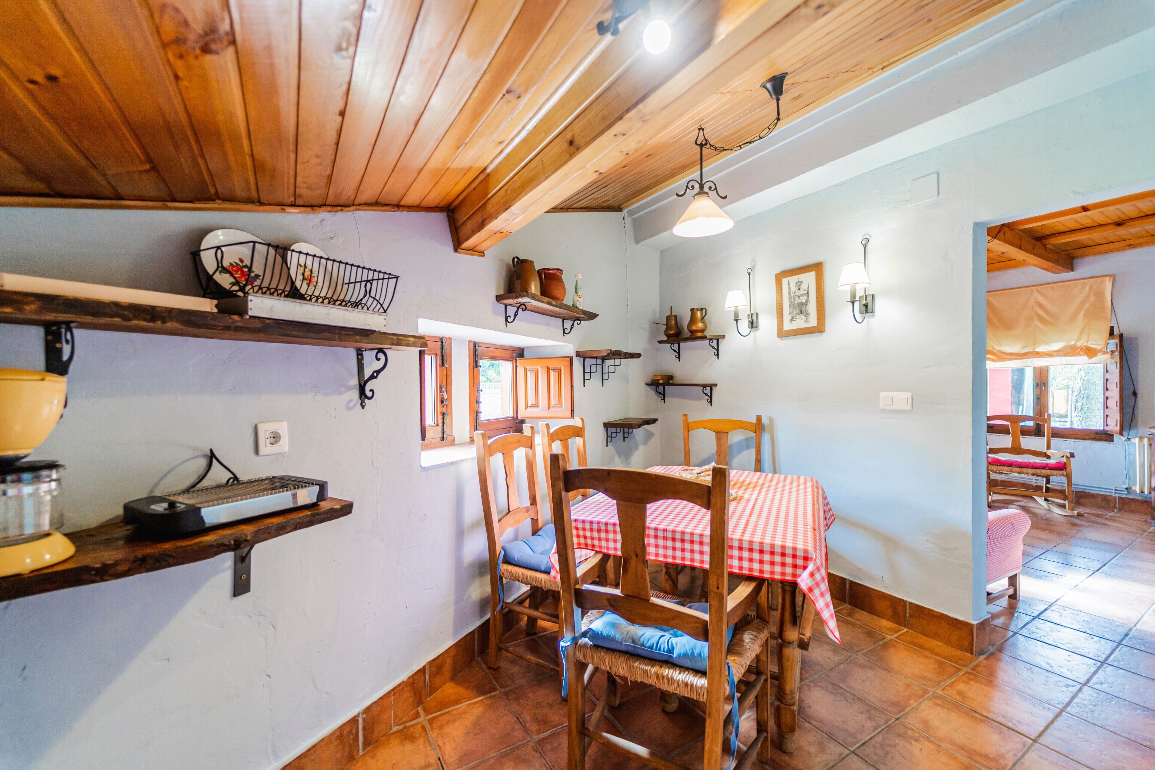 Un'area pranzo rustica con mobili in legno, una tovaglia a quadri ed scaffali pieni di stoviglie.