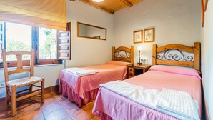 Una habitación con dos camas, una silla de madera, una ventana con persianas, un espejo y un cuadro colgado en la pared.
