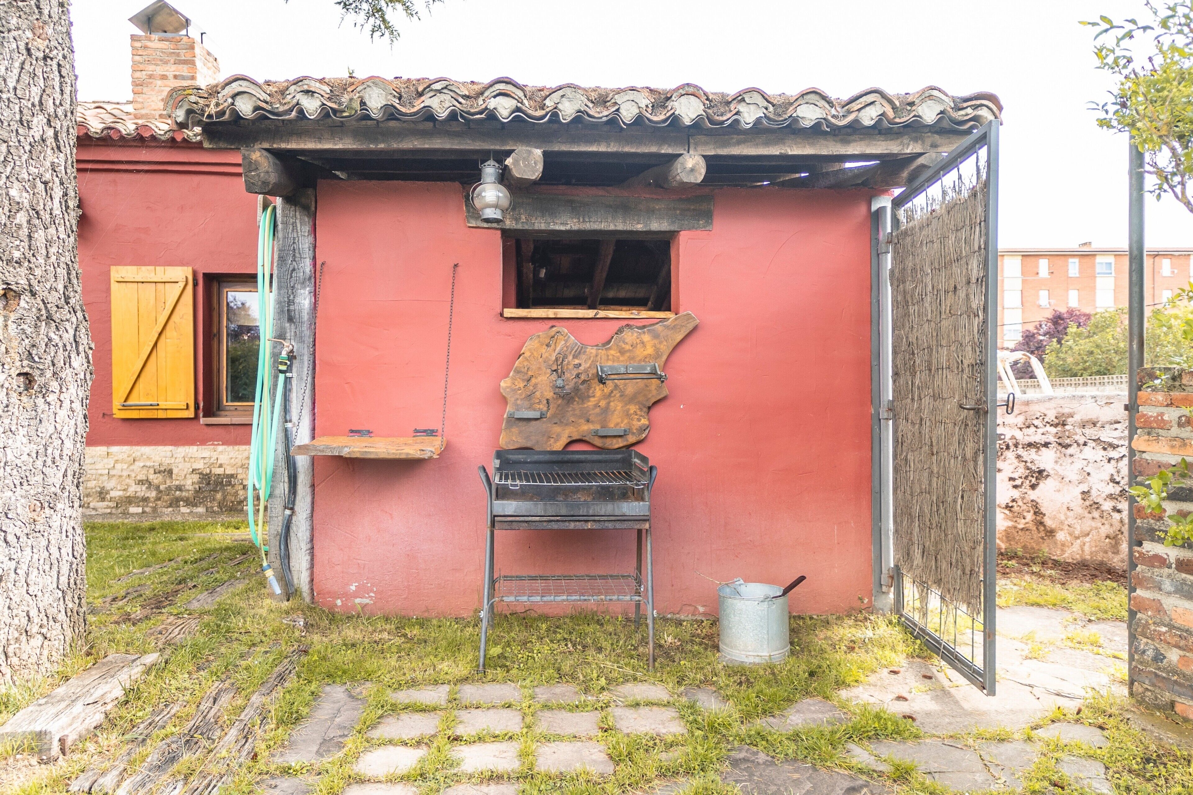 Eine kleine Gartenlaube mit Ziegeldach, Grill und Metalleimer.