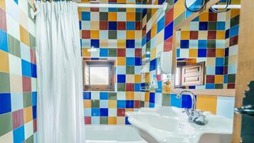 Un baño con pared de mosaicos de colores, un lavamanos blanco, una bañera y una cortina de ducha.