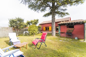 A backyard with a red building, a tree, and two lounge chairs.
