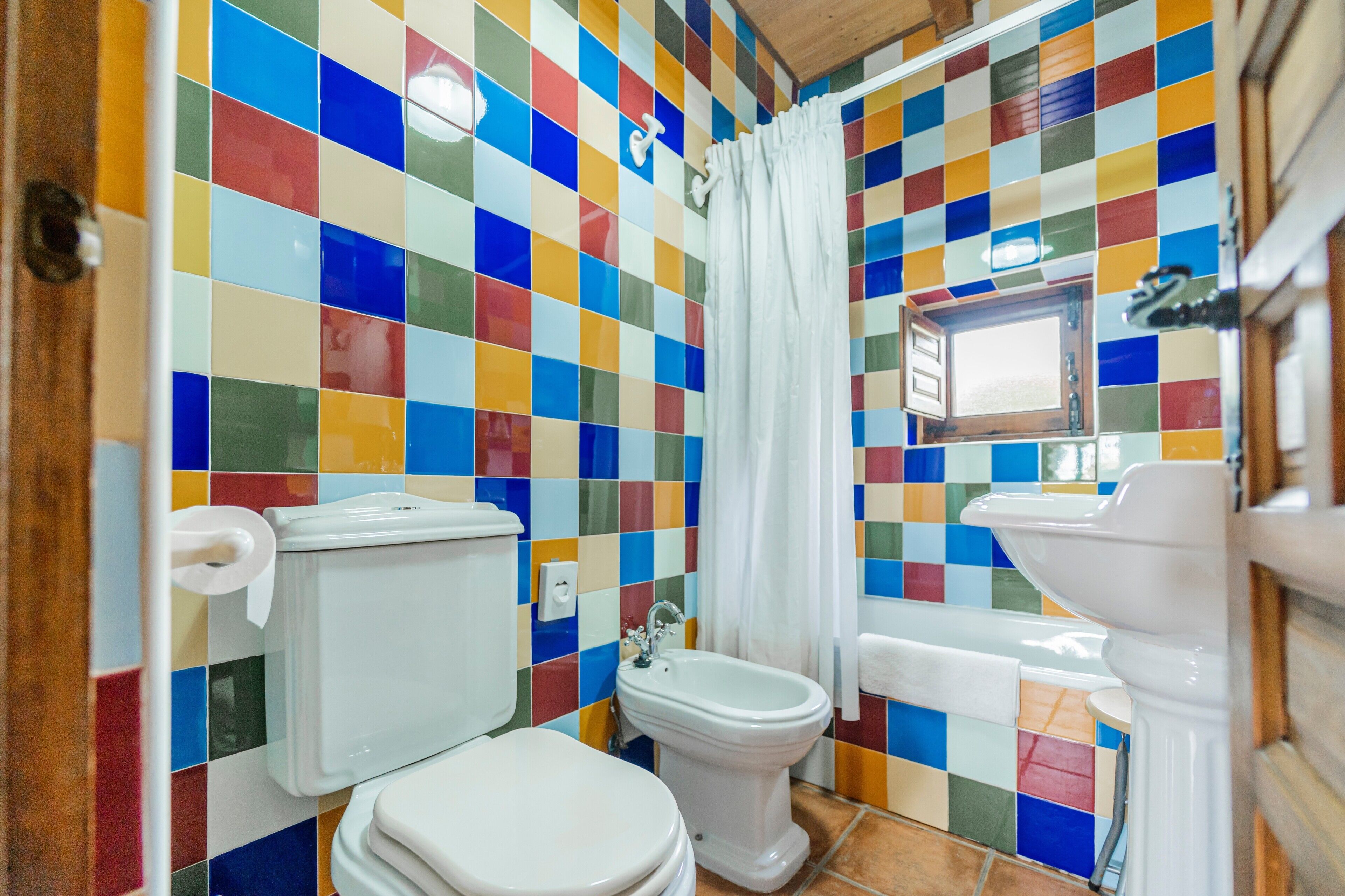 Un baño con una pared de azulejos de colores, un inodoro, un bidé y un lavabo.