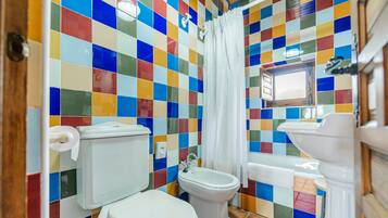 Un baño con una pared de azulejos de colores, un inodoro, un bidé y un lavabo.