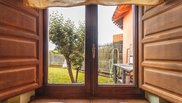 Una panchina di legno con vista su un giardino, visibile attraverso un'apertura: si vedono un albero e un recinto.