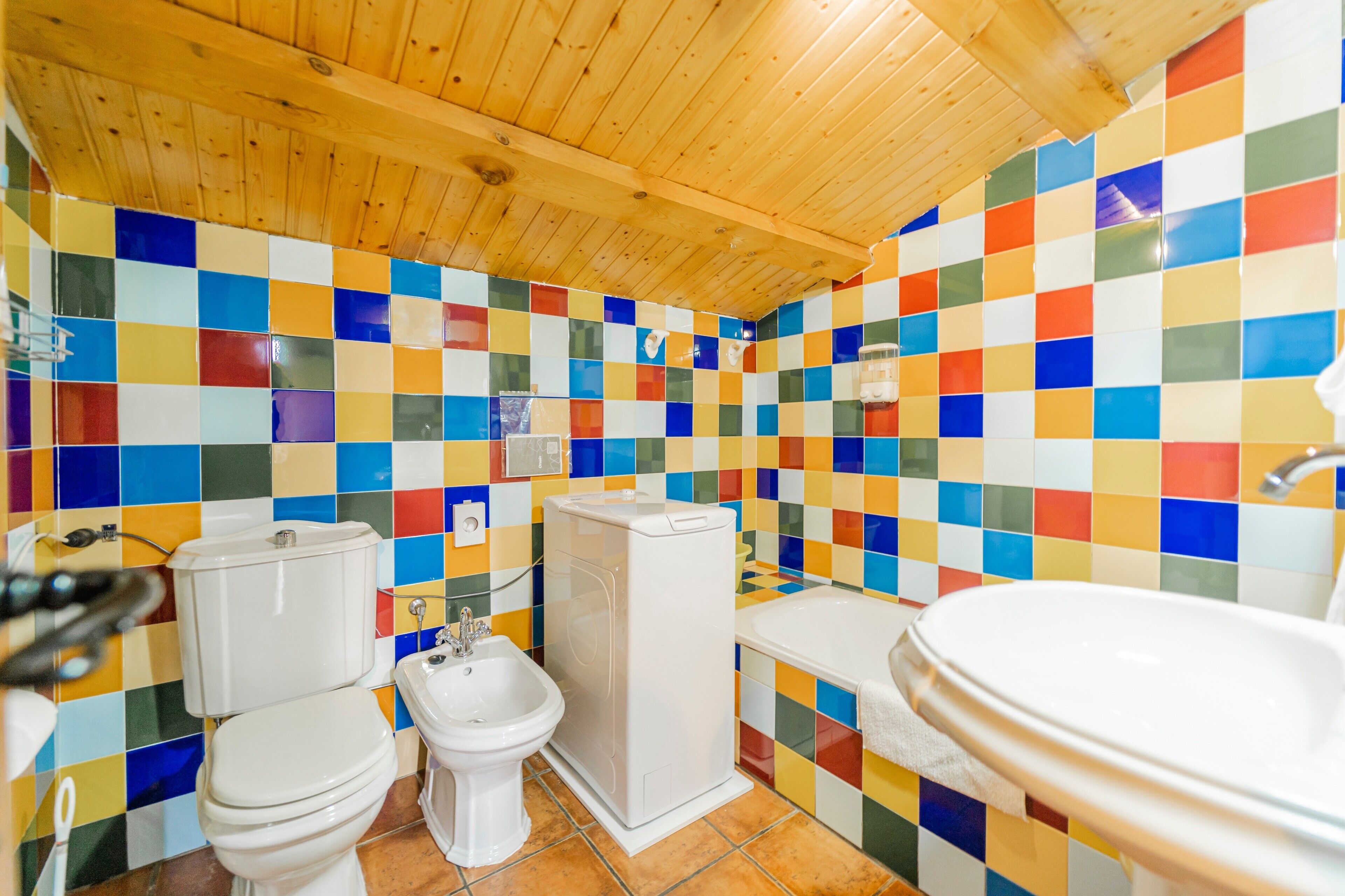 A bathroom with a tiled wall, a wooden ceiling, a toilet, a bidet, and a sink.