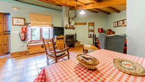 Una stanza accogliente con soffitto in legno, un camino, una televisione, un tavolo da pranzo con tovaglia a quadri e un arredamento rustico che include una testa di cervo.