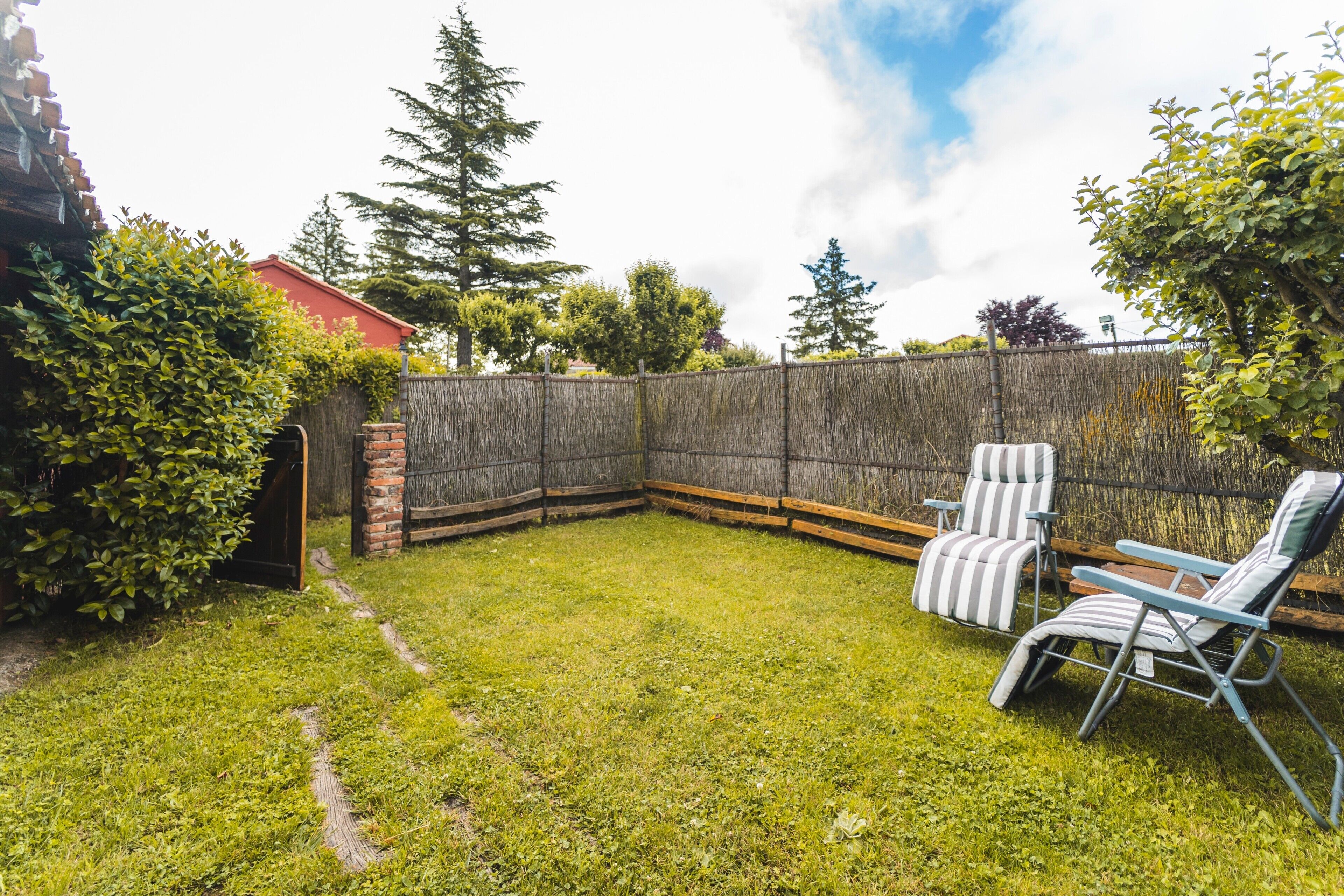 A backyard with a wooden fence, two striped lawn chairs, and a brick wall.