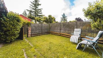 A backyard with a wooden fence, two striped lawn chairs, and a brick wall.