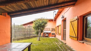 Un'area patio con tavolo e sedie, un piccolo albero e un edificio dalle pareti arancioni e persiane in legno.