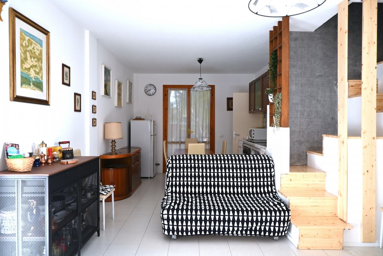 En stue med sofa, spisebord, et køkken og en trappe.