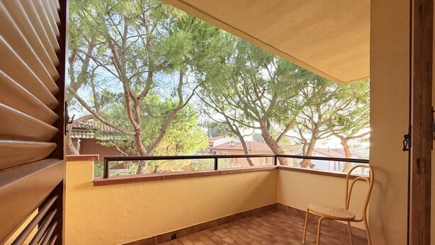 Varanda com vista para árvores e casas, uma cadeira e piso de azulejos.