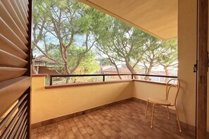 Un balcon donnant sur des arbres et des maisons, une chaise et un sol carrelé.