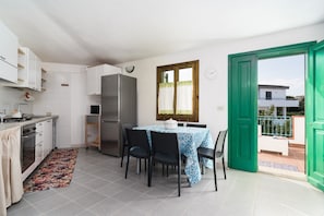 Cocina compacta con zona de comedor, refrigerador y ventana con cortinas.