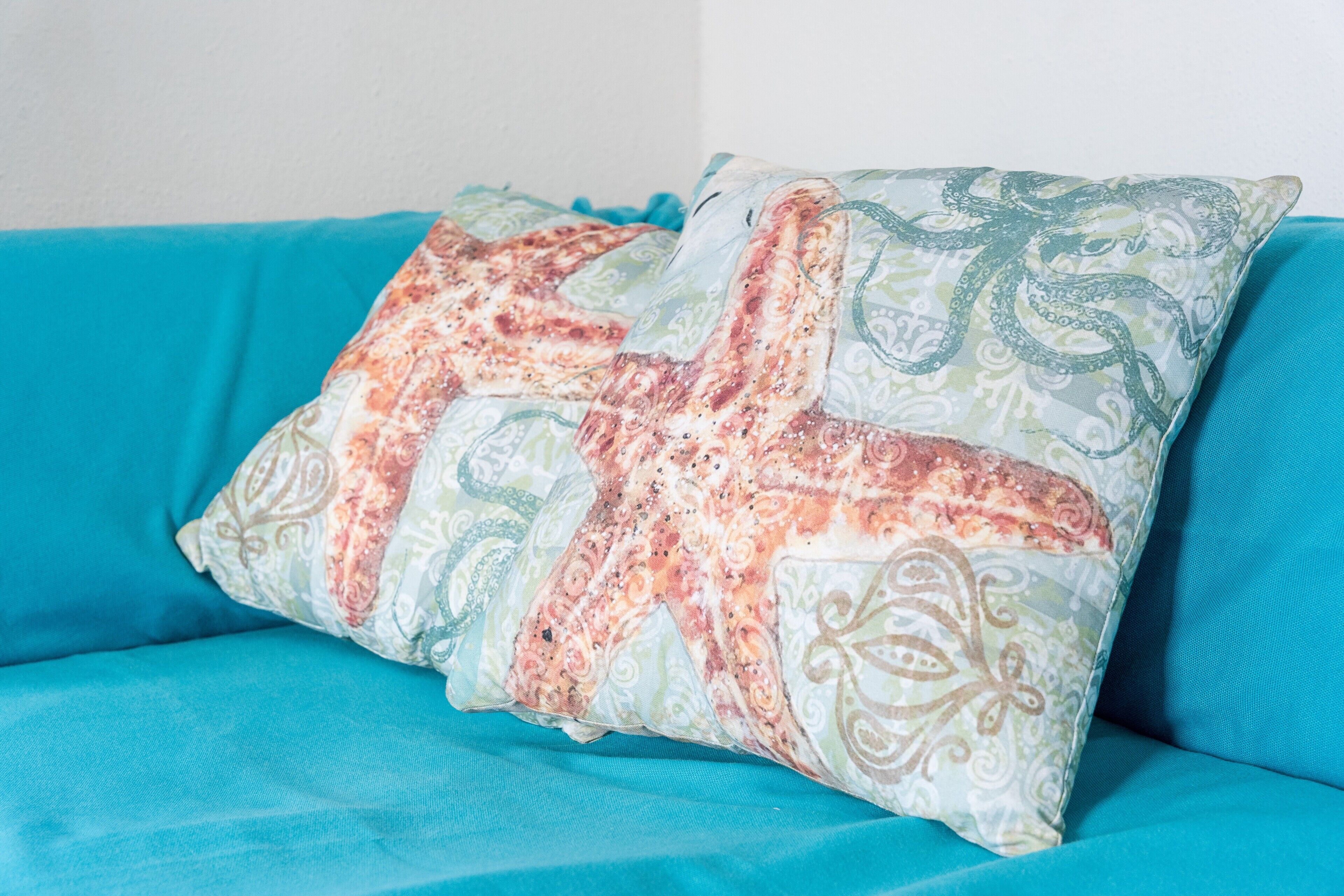 A teal sofa with a decorative pillow featuring an octopus design.