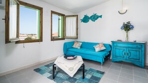 Une pièce avec un canapé bleu, une petite table sur laquelle se trouve un bol, un meuble et deux fenêtres avec des rideaux.