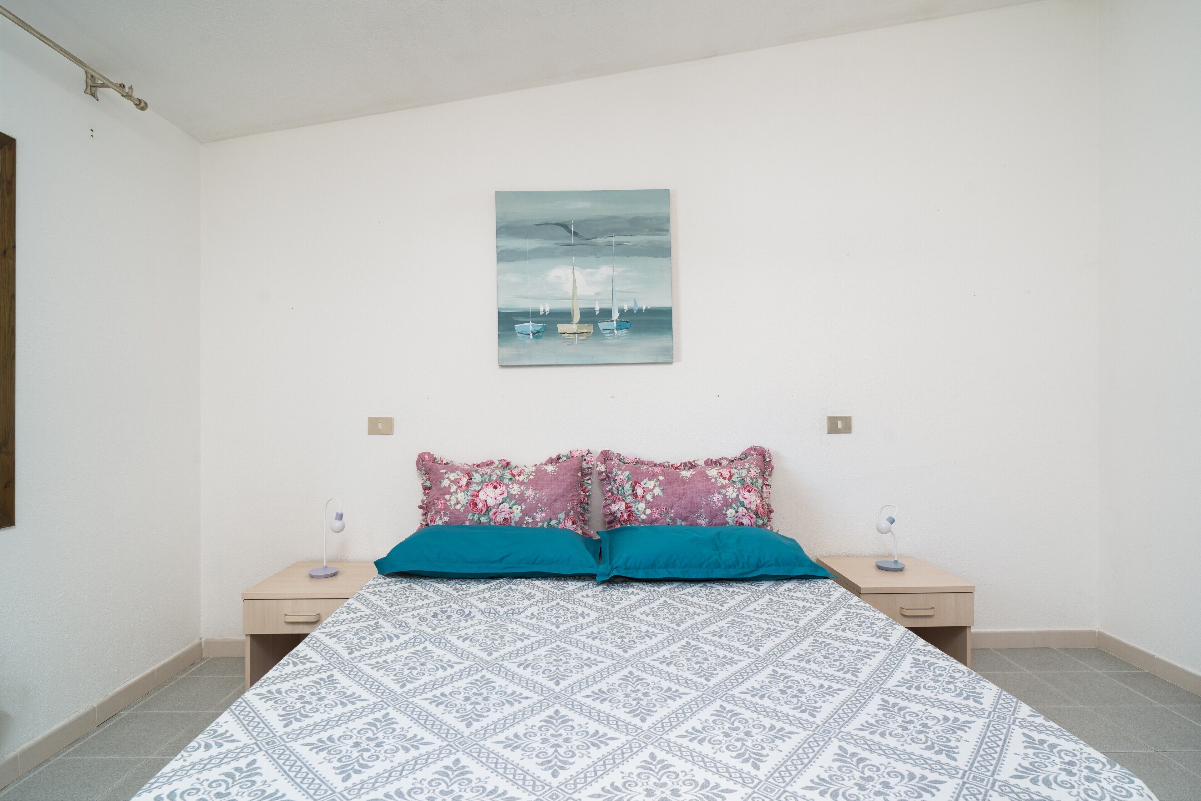 A bedroom with a bed, two bedside tables, a wall-mounted painting, and a patterned bedspread.