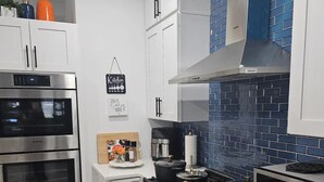 Eine moderne Küche mit weißen Schränken, einem Bosch-Ofen, einer Panasonic-Mikrowelle und einer blau gefliesten Spritzschutzwand.