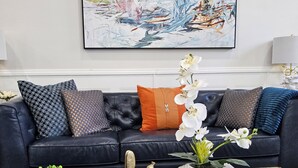 Ein modernes Wohnzimmer mit einem schwarzen Ledersofa, einem Glastisch und einem großen abstrakten Gemälde an der Wand.
