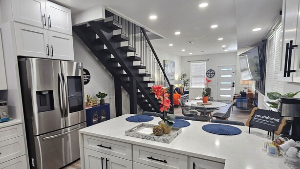 Eine moderne Küche mit weißen Schränken, einem Edelstahl-Kühlschrank, einer schwarzen Treppe und einem Essbereich mit blauen Platzsets.