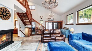 A spacious living room with a fireplace, leather armchair, blue sofa, and a chandelier. - NEW The Hamilton Chalet: Private Hot Tub, Seclusion, & Incredible Mtn Views! (Breckenridge)