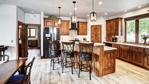 A modern kitchen with wooden cabinets, a central island with bar stools, stainless steel appliances, and pendant lighting. - NEW The Hamilton Chalet: Private Hot Tub, Seclusion, & Incredible Mtn Views! (Breckenridge)