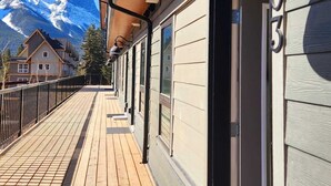Una terraza de madera con barandilla de metal, un ventanal y vista a la montaña.