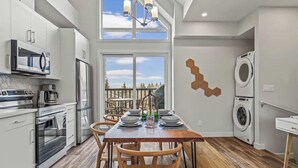 Una cocina moderna con armarios blancos, una mesa de comedor preparada para cuatro personas y un ventanal con vistas al exterior.