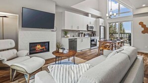 Una sala de estar moderna con chimenea, televisor y comedor, iluminada por luz natural que entra por amplias ventanas.