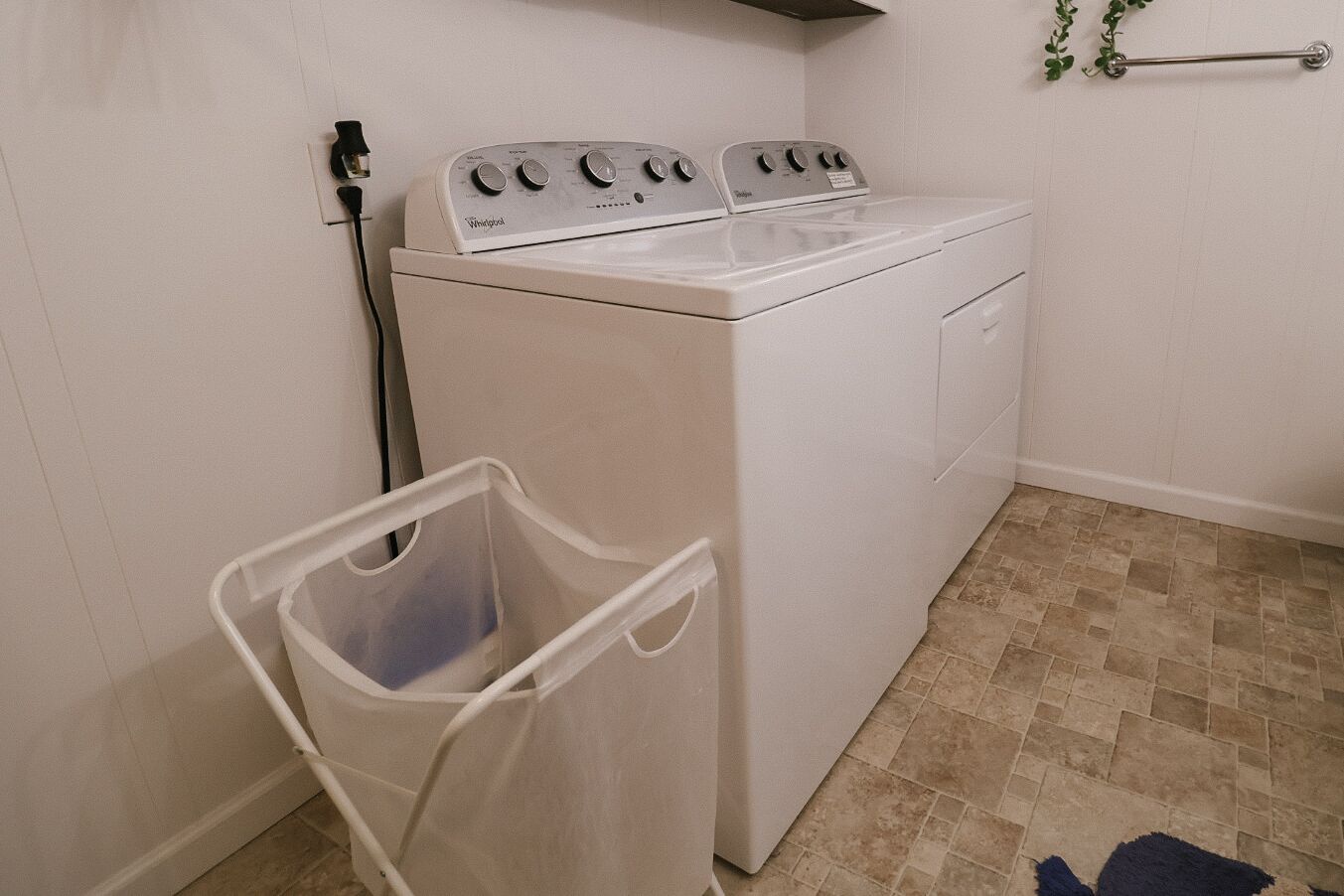 A compact laundry room with a front-loading washer and dryer, a small trash bin, and a metal towel rack.
